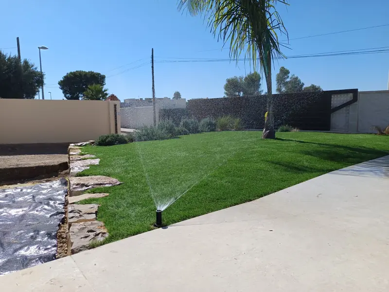 Riego por aspersores emergentes en pradera de césped junto a la piscina